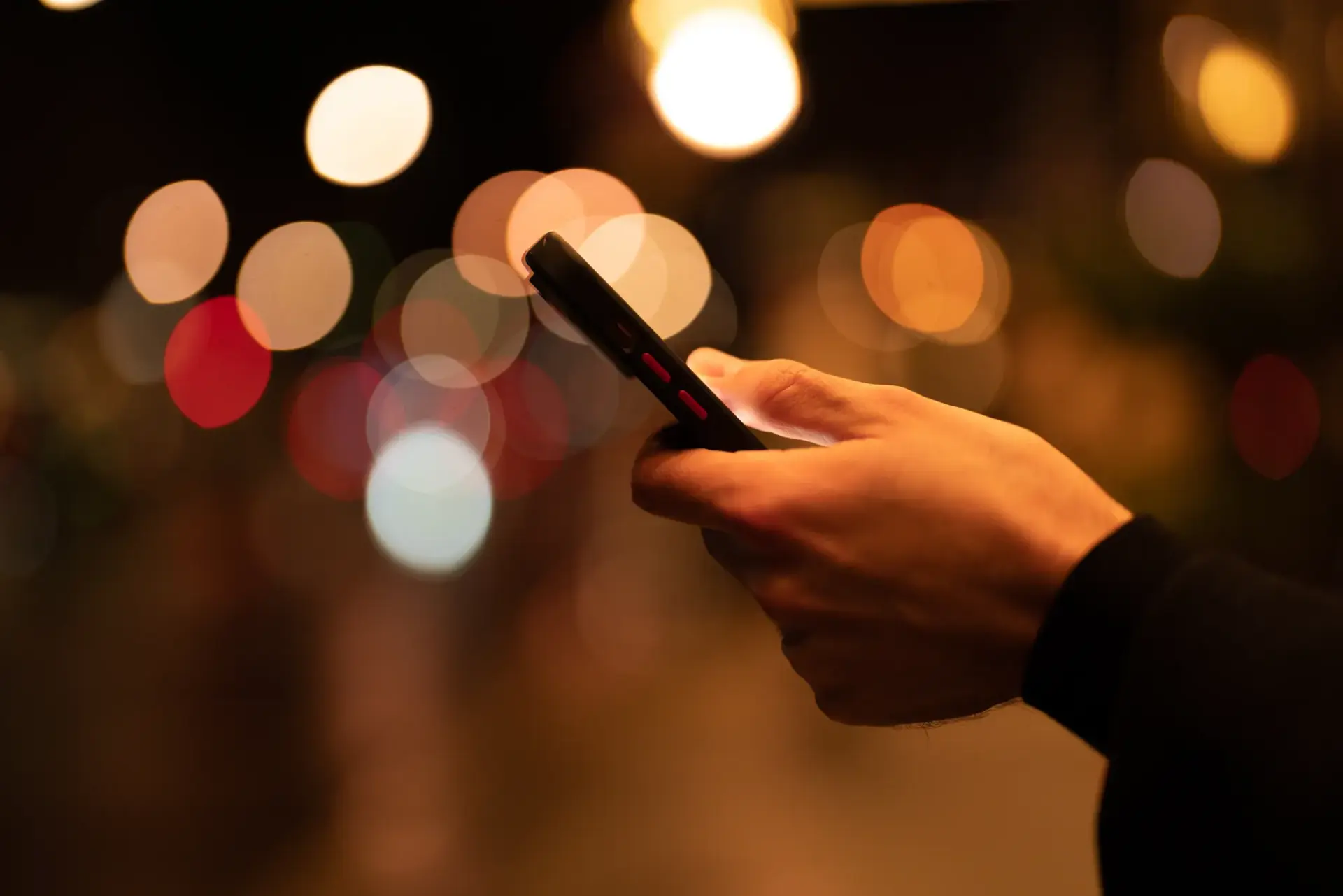 Main tenant un téléphone devant les lumières de la ville, la nuit